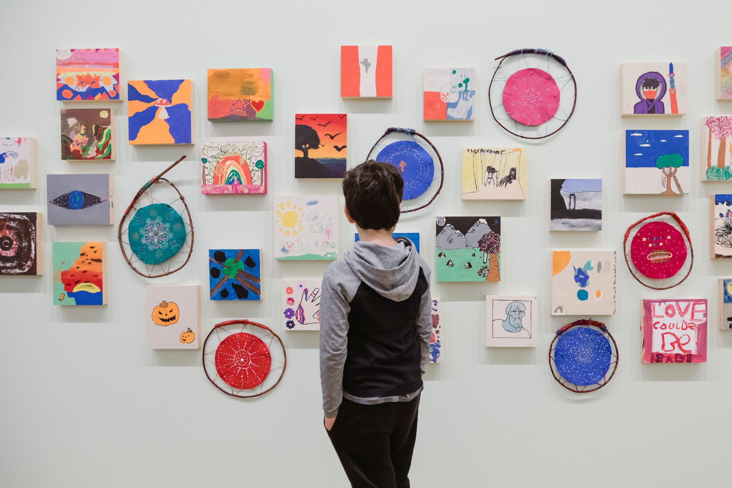 A child looks at student art on the wall of a museum gallery