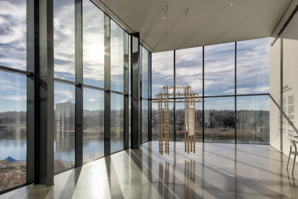A wooden artwork in the shape of gate hangs in the museum with sunlight coming through the windows