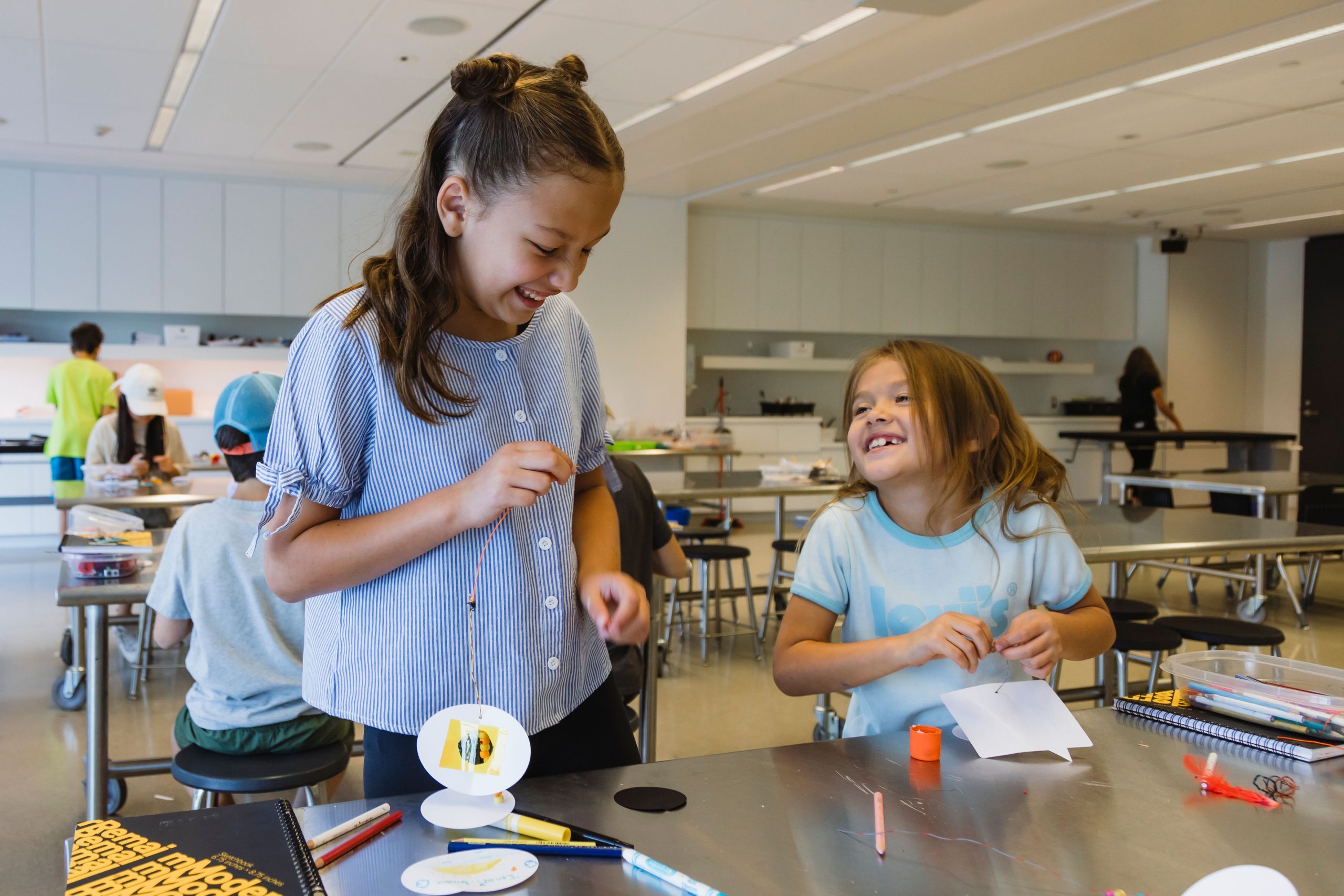 Two children smile at one another as they make art in Remai Modern's learning studio.