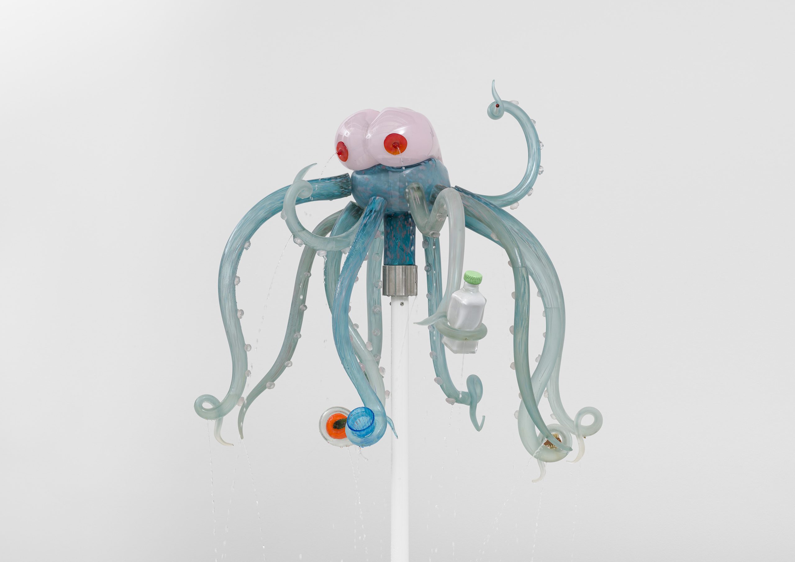 A Venetian glass sculpture depicts an octopus-like creature with breasts for a head. The creature is grasping various items in its tentacles including an orange and a glass.