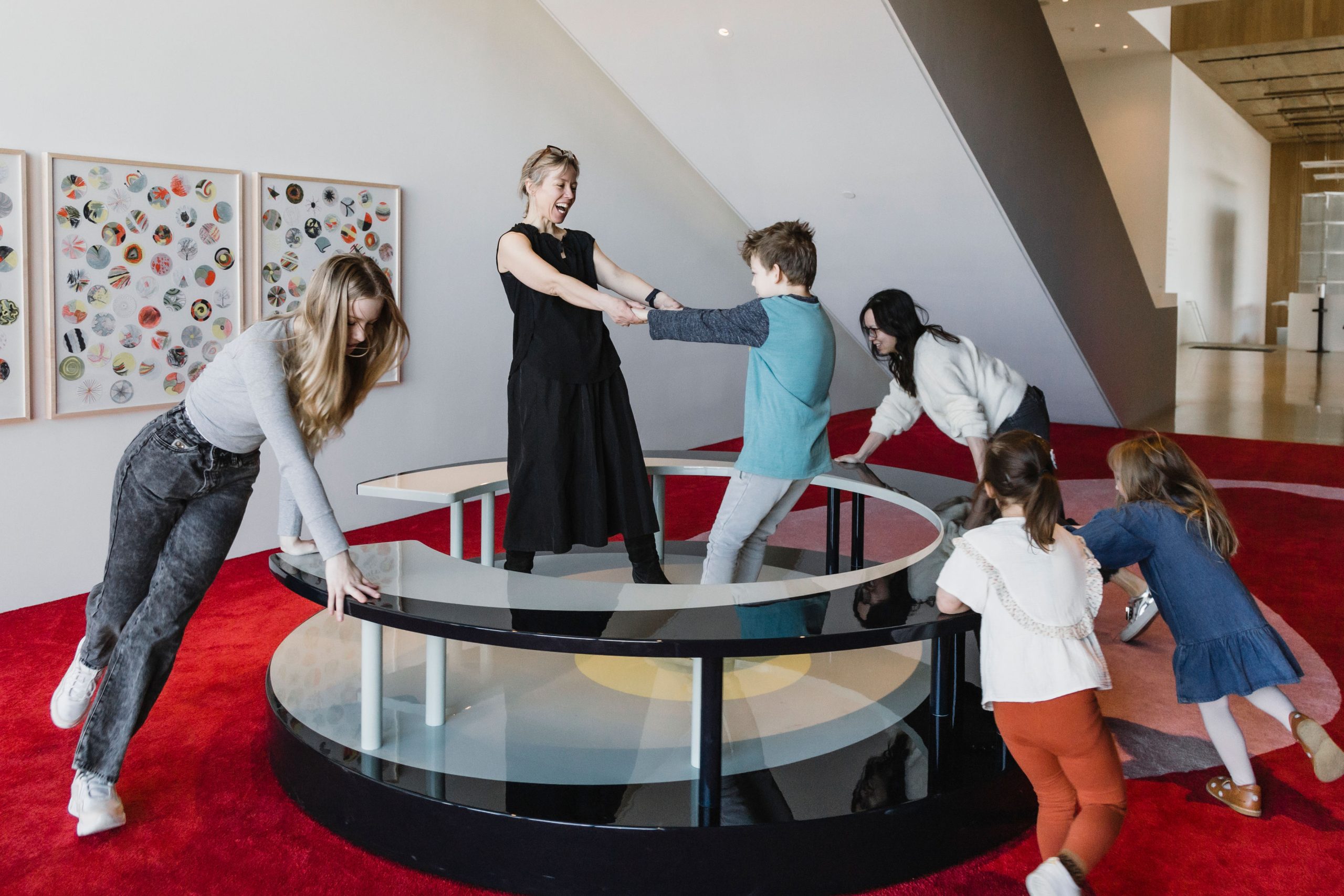 A group of people play on a large carousel underneath a stair case