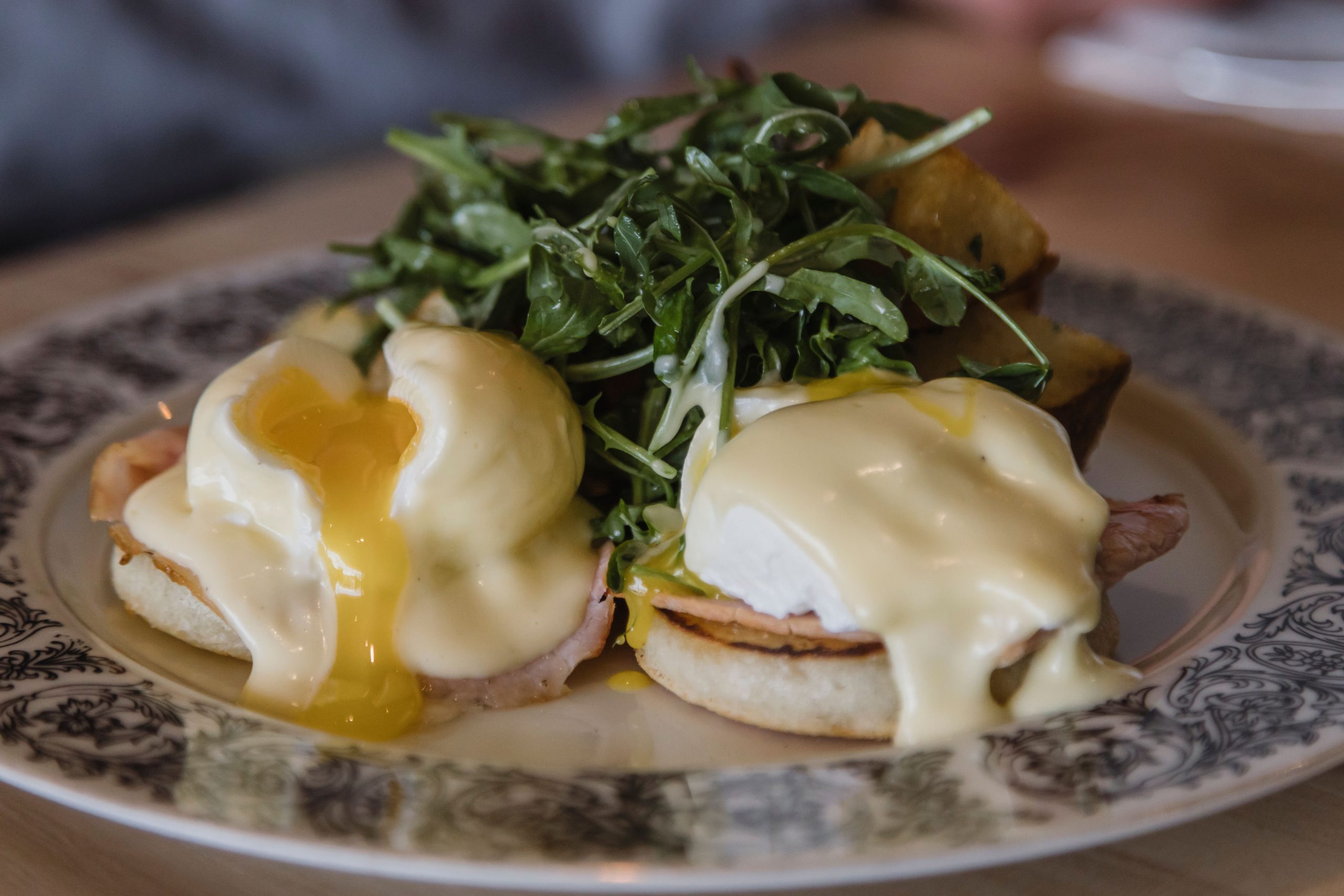Eggs benedict with soft yolk and hollandaise sauce, topped with arugula