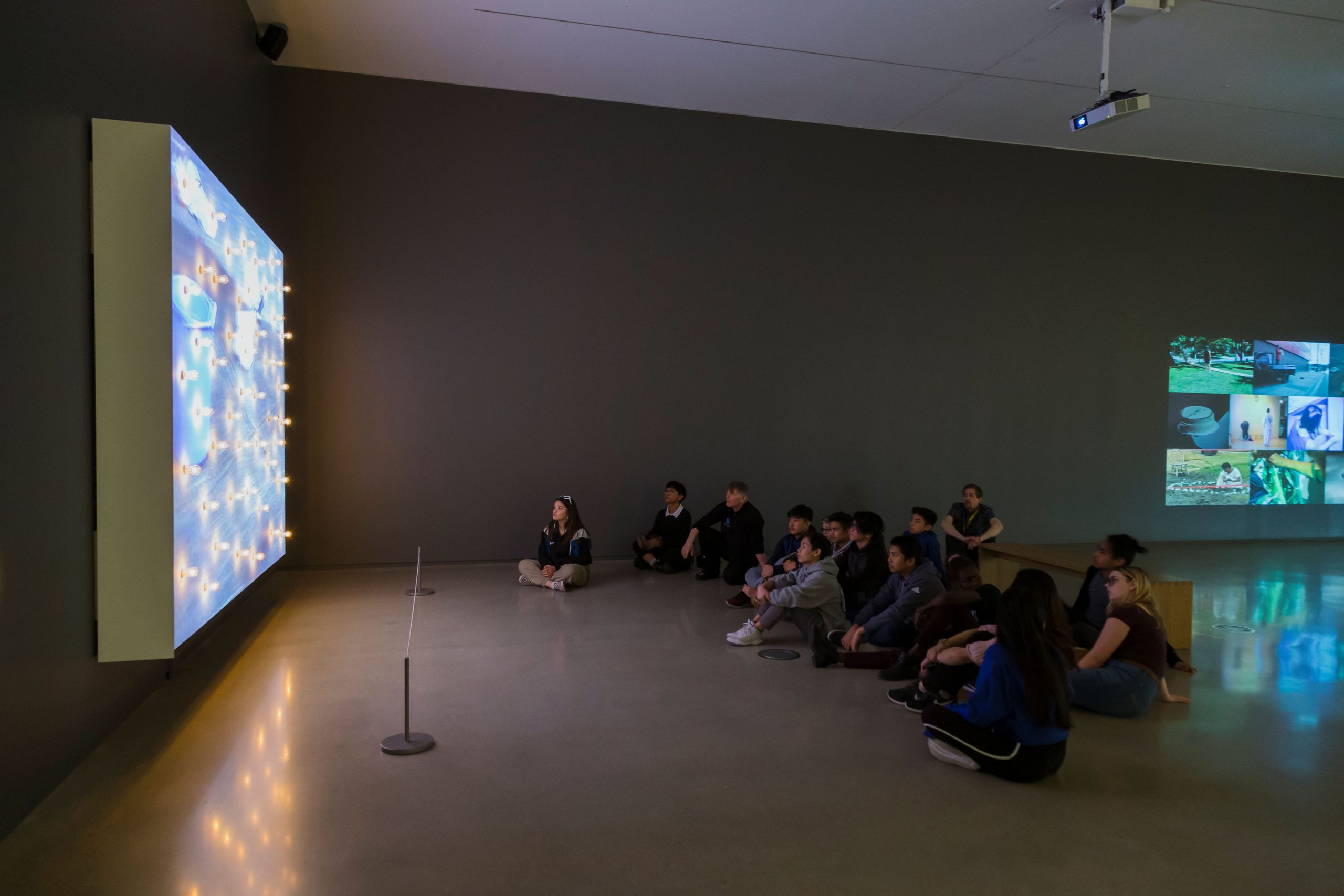 A group of students watch a media artwork in an art gallery