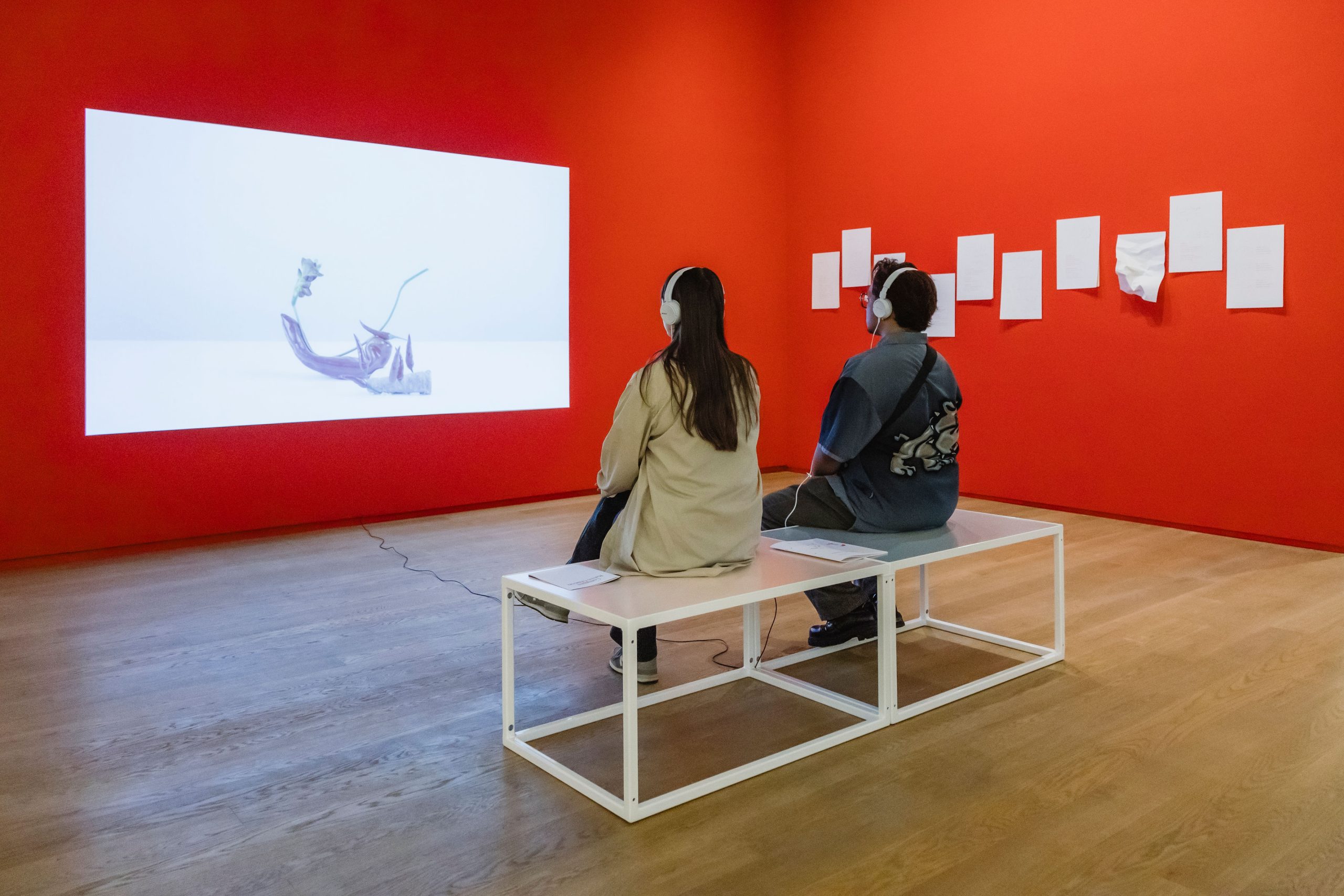 Two people sit on a bench as they watch a video work.