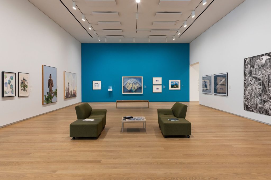 A room in the Collection Galleries, with artworks on three walls and a seating area in the middle.