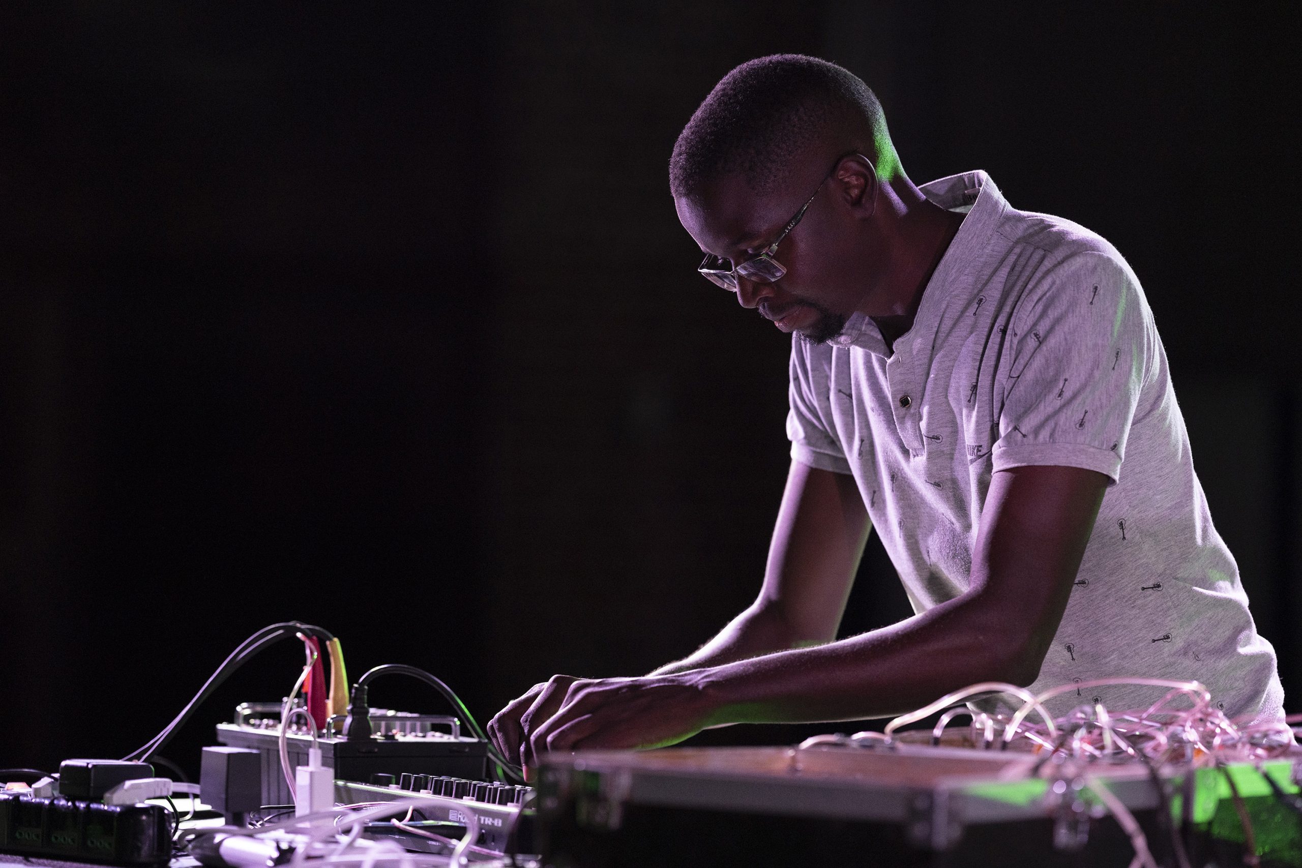 A person operating an electronic music equipment on a table, adjusting various knobs and cables.