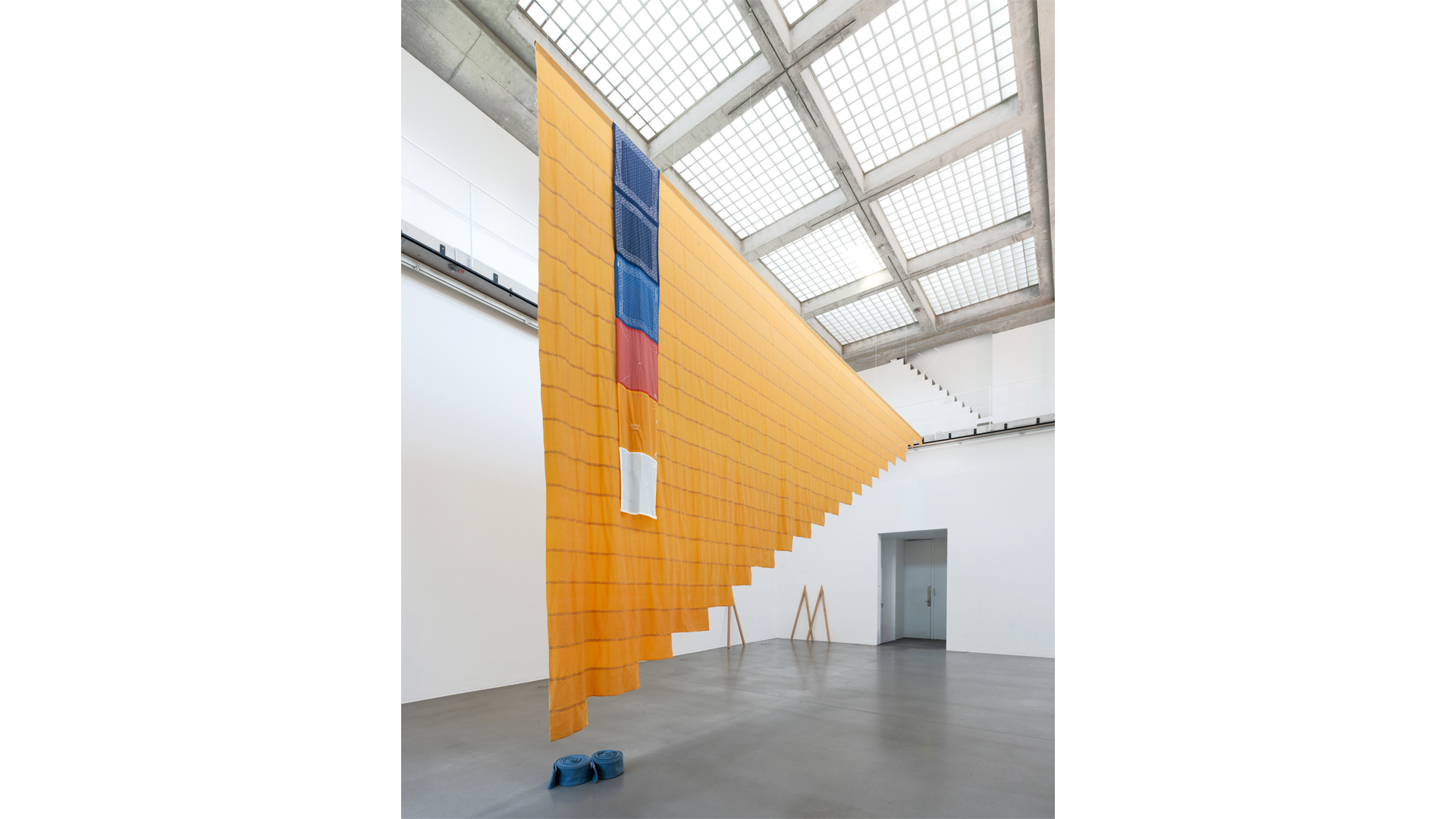 Large suspended textile installation in a bright gallery, with long translucent orange fabric panels hanging diagonally from the ceiling. Tanya Lukin Linklater, Crested, 2026, Installation view, Crested, Portikus, Frankfurt am Main, 2026. Courtesy of the artist. Photo: Robert Schittko